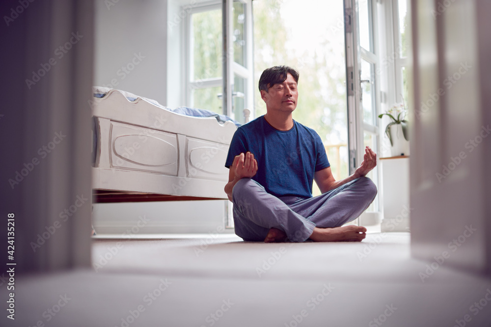 Mature Asian Man In Pyjamas Sitting On Bedroom Floor Meditating In Yoga Pose Mature Asian Man In Pyjamas Sitting On Bedroom Floor Meditating In Yoga Pose