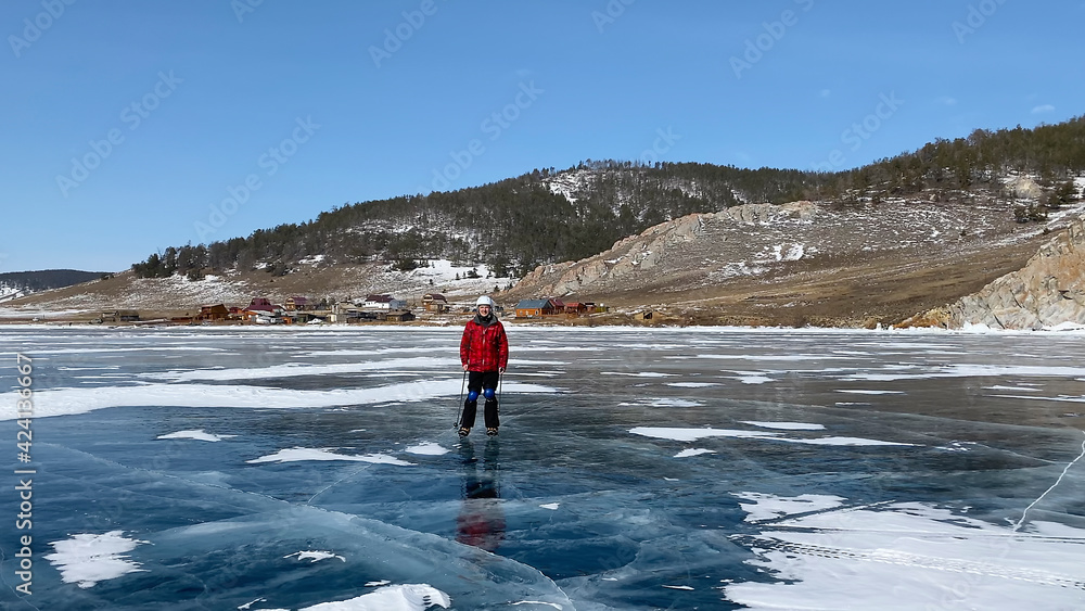 A guy in a white helmet, ice skates, knee pads and with ski poles is rolling on the ice of frozen Lake Baikal.