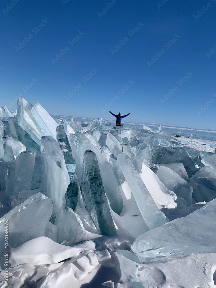 Happy tourist sits on the ice troughs of Lake Baikal. Large, impenetrable chunks of ice.