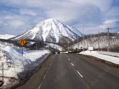 Snow-capped volcano beyond a road (Mount Yotei, Hokkaido, Japan)