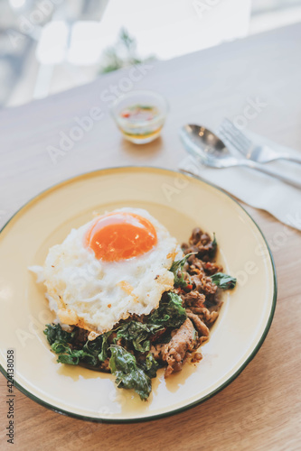 Thai food (Stir Fried Basil, Pork, Fried Egg), Stir Fried Basil with Minced Pork, Fried Egg, Topped on Steamed Rice in a Zinc Plate on a Wooden Table,closeup