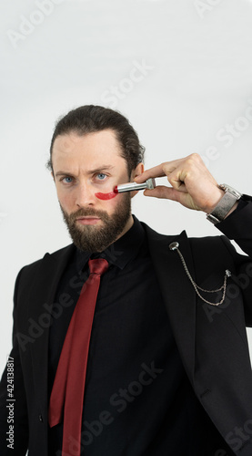 fashion shooting of a young man in a business suit and lipstick in hand