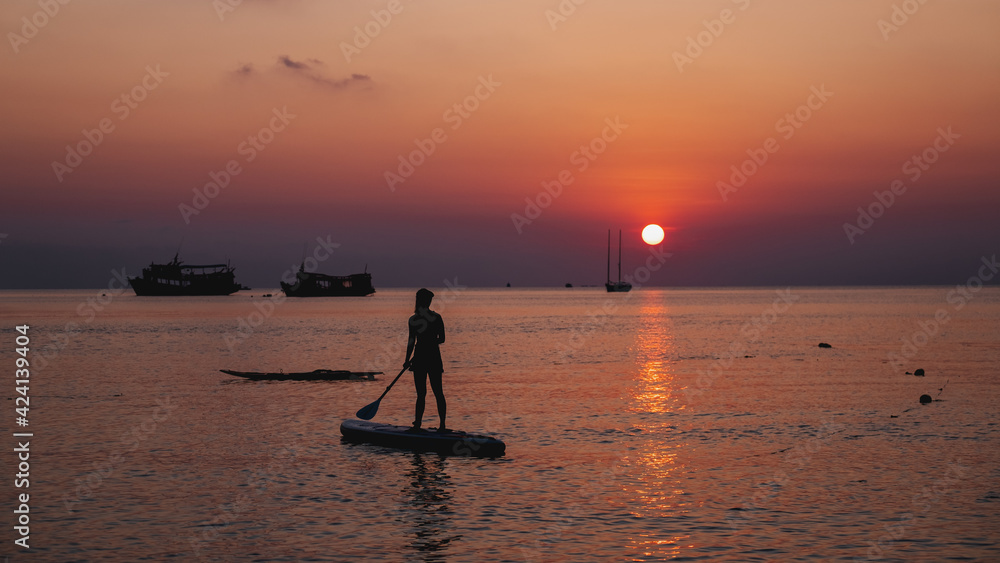 Silhouette image of a young woman on stand up paddle board in the sea before sunset