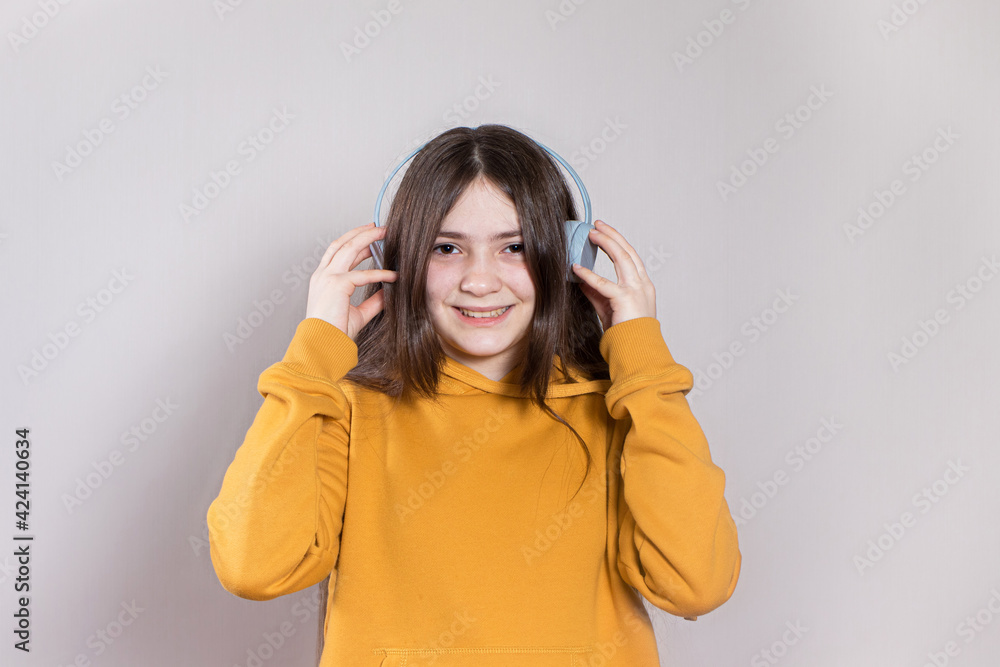 A teenage girl with long dark hair smiles and laughs in a bright orange hoodie in headphones listening to music with place for text and copy space. A teenage girl with long dark hair smiles and laughs in a bright orange hoodie in headphones listening to music with place for text and copy space.