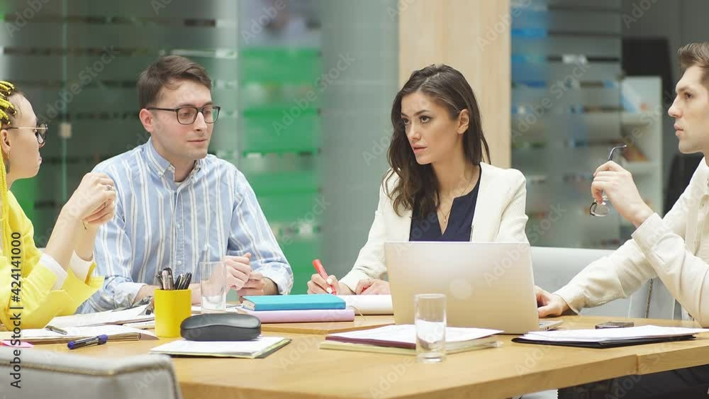 Several employees in the office at a desk. Young people in stylish casual clothes sit at a desk in the office and discuss business Several employees in the office at a desk. Young people in stylish casual clothes sit at a desk in the office and discuss business