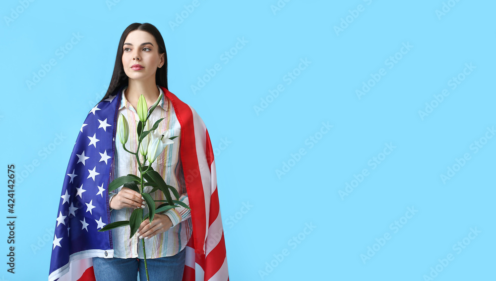 Fototapeta premium Young woman with USA flag and flowers on color background. Memorial Day celebration