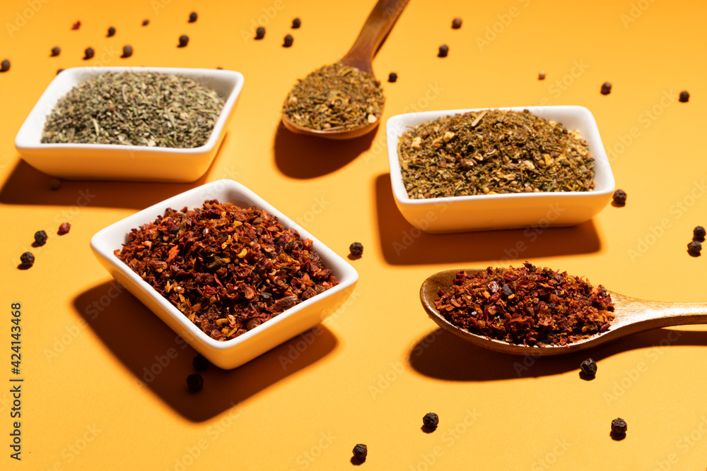 Collection of three spices on wooden spoons and white bowls on orange background,top view.Flat lay