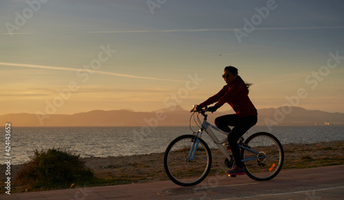 Woman in sports suit, rides a bicycle, in front of the sea, at sunset