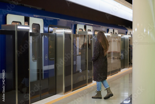 A full-length photo of a woman in a medical face mask to avoid the spread of coronavirus who is going to the modern subway car. A girl in a surgical mask is keeping social distance on a metro station.