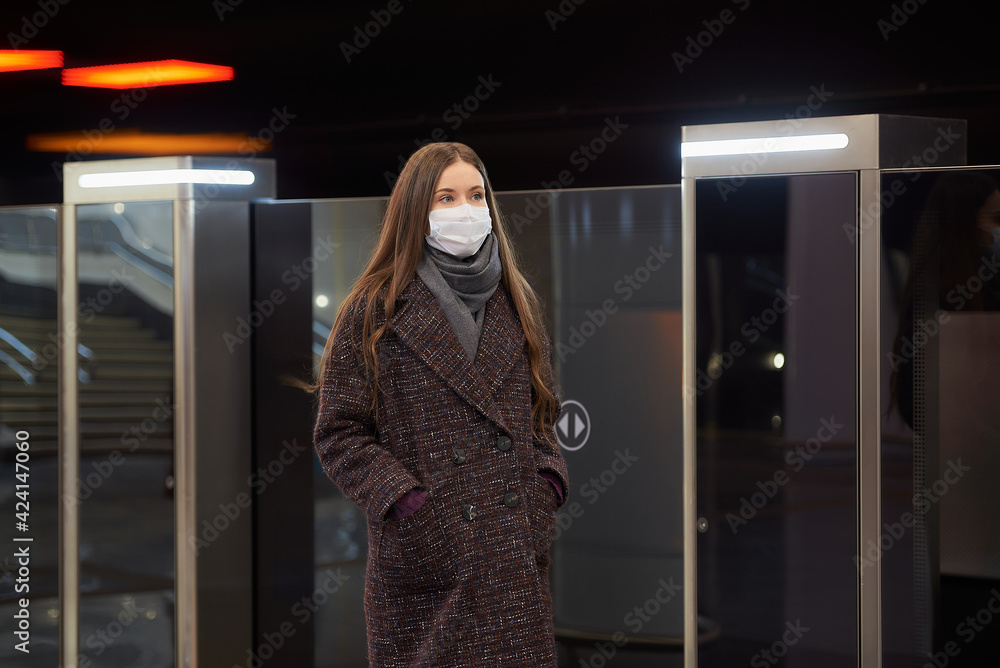 A woman in a medical mask to avoid the spread of coronavirus is standing near the departing train on the subway platform. A girl in a surgical mask is keeping social distance on a metro station. A woman in a medical mask to avoid the spread of coronavirus is standing near the departing train on the subway platform. A girl in a surgical mask is keeping social distance on a metro station.