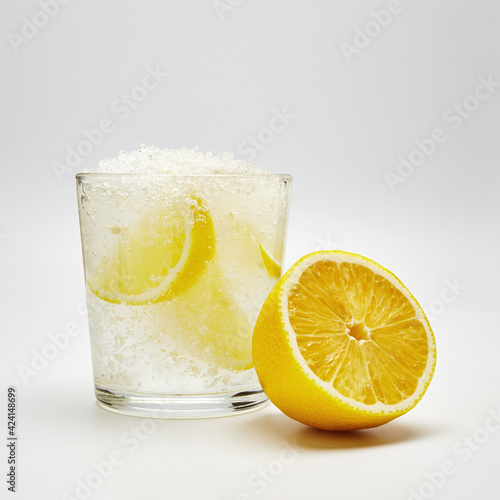 water with lemon and ice in a glass glass near half a lemon on a light background close-up