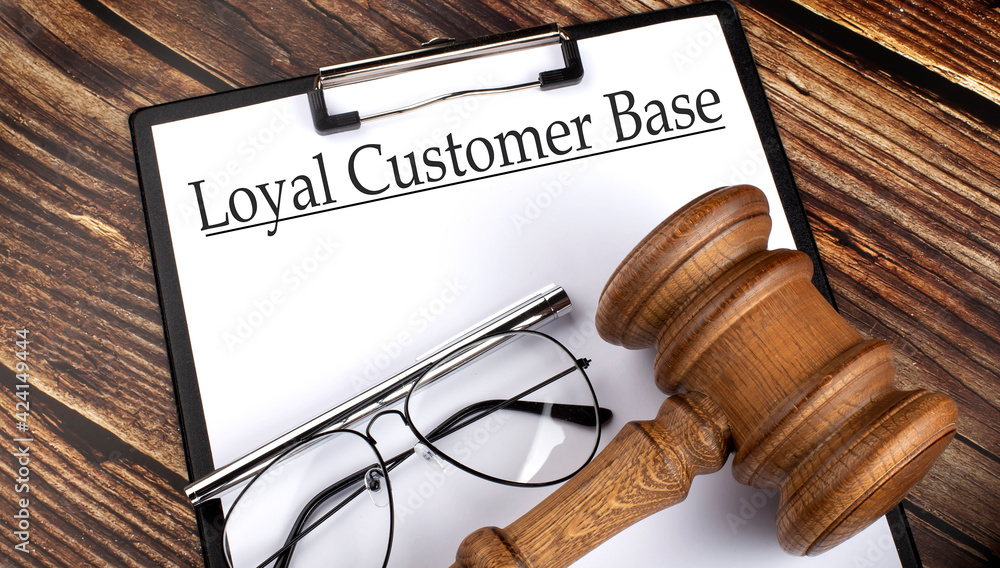 Paper with LOYAL CUSTOMER BASE with gavel, pen and glasses on the wooden background Paper with LOYAL CUSTOMER BASE with gavel, pen and glasses on the wooden background