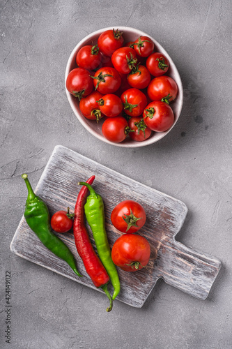 Fresh ripe tomatoes in bowl near to old wooden cutting board with hot chili peppers  stone concrete background  top view