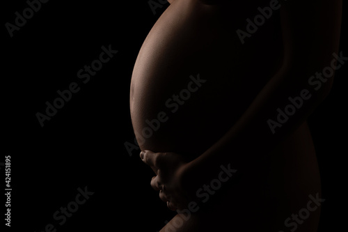 Pregnant girl in the dark, low key. Black background.