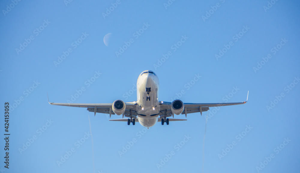the airliner with landing gear lands against the background of the off runway lights against the background of a clear sky and against the moon during the day 