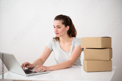 A European woman places an order in a laptop for goods packed in boxes. place to advertise the product of production.