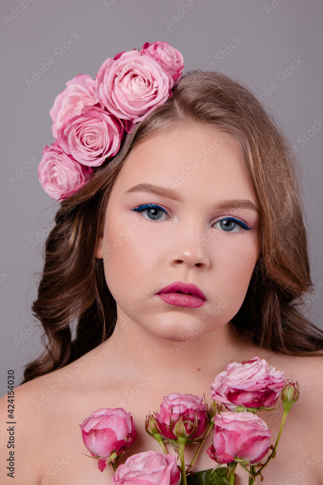 brunette teenage girl with pink roses in her hair on gray background. flowers in curls on the head. fashion photo brunette teenage girl with pink roses in her hair on gray background. flowers in curls on the head. fashion photo