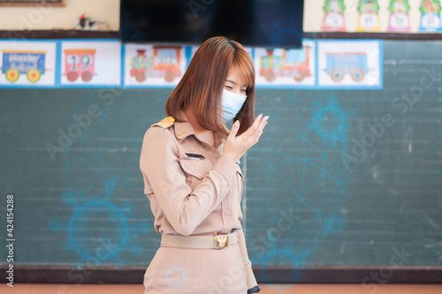 Female thai teacher in uniform standing in front of the classroom wearing mask  coughing with virus around her