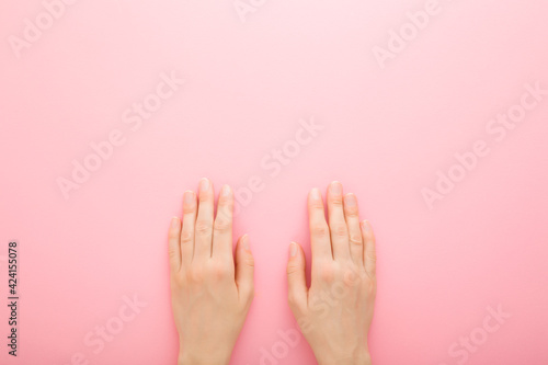 Young adult woman hands on light pink table background. Pastel color. Closeup. Point of view shot. Care about clean, beautiful, soft hands skin and nails. Empty place for text. Top down view.