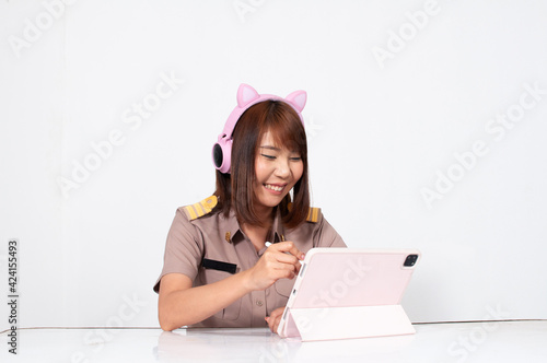 Female thai teacher in uniform sitting with white background writing on tablet with headphones on
