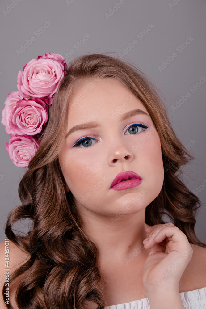 portrait of pretty brunette girl with pink roses in her hair on gray background. flowers in curls on the head. spring, flowering, colors. fashion photo portrait of pretty brunette girl with pink roses in her hair on gray background. flowers in curls on the head. spring, flowering, colors. fashion photo