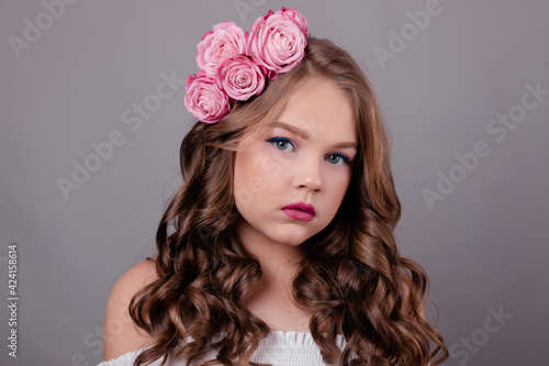portrait of pretty brunette girl with pink roses in her hair on gray background. flowers in curls on the head. spring, flowering, colors. fashion photo
