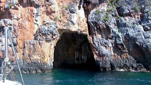 Boat going to enter a large cave in the jagged cliff along Marina di Camerota coastline, Italy. photo