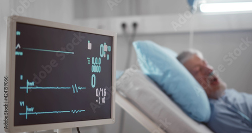 Fototapeta Portrait of senior man in coma dying in hospital bed with heart rate falling on ecg monitor