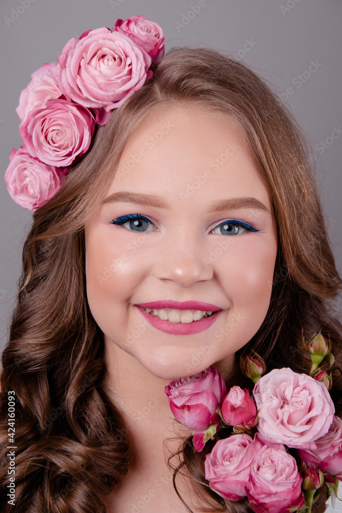 brunette teenage girl with pink roses in her hair on gray background. flowers in curls on the head. fashion photo brunette teenage girl with pink roses in her hair on gray background. flowers in curls on the head. fashion photo