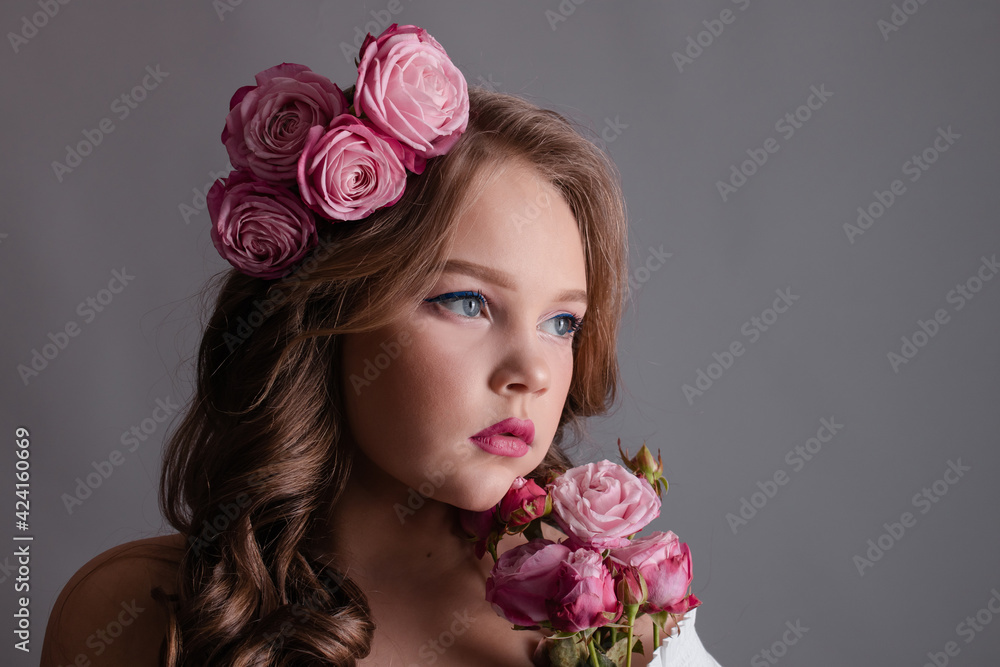 brunette teenage girl with pink roses in her hair on gray background. flowers in curls on the head. fashion photo brunette teenage girl with pink roses in her hair on gray background. flowers in curls on the head. fashion photo