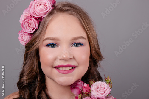 portrait of pretty brunette girl with pink roses in her hair on gray background. flowers in curls on the head. spring, flowering, colors. fashion photo © OliaVesna