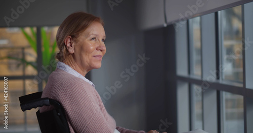 Mature woman sitting in wheelchair in nursing home looking out of window photo