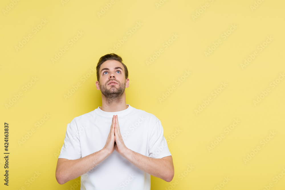 young man looking up while showing hope gesture on yellow young man looking up while showing hope gesture on yellow