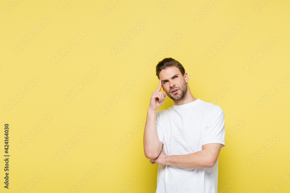 pensive man looking away and touching head while standing on yellow pensive man looking away and touching head while standing on yellow