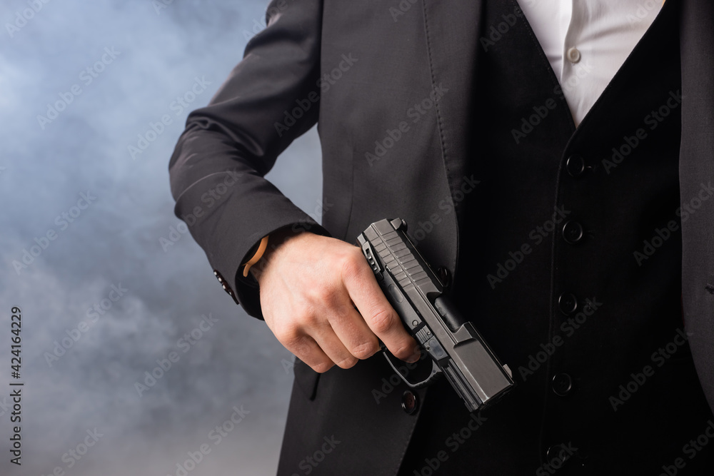 partial view of businessman with gun on grey background with smoke - obrazy, fototapety, plakaty 