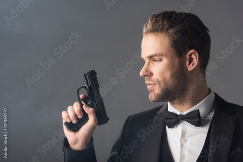 young, confident businessman holding weapon on grey background with smoke photo