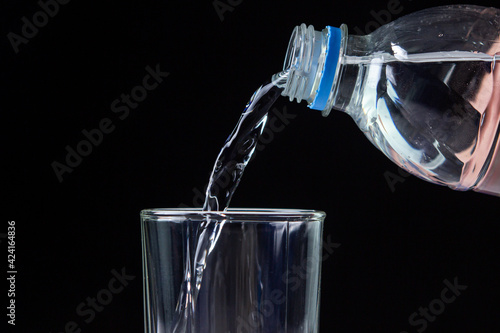 Water is poured from a bottle into a glass. Clean drinking water. Water on black background