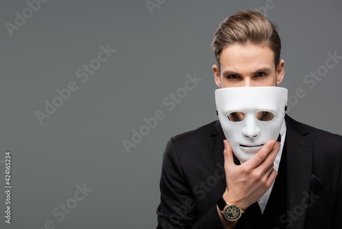 businessman holding mask near face while looking at camera isolated on grey