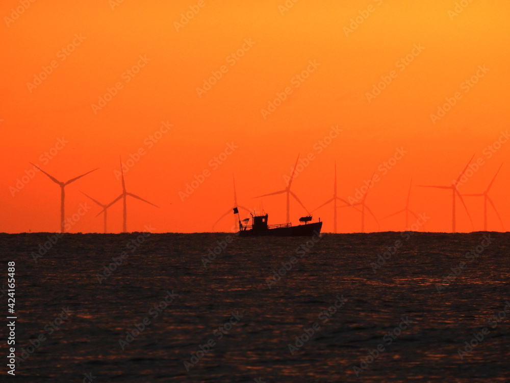The contours of a small fishing boat in the morning at sea with an orange sky