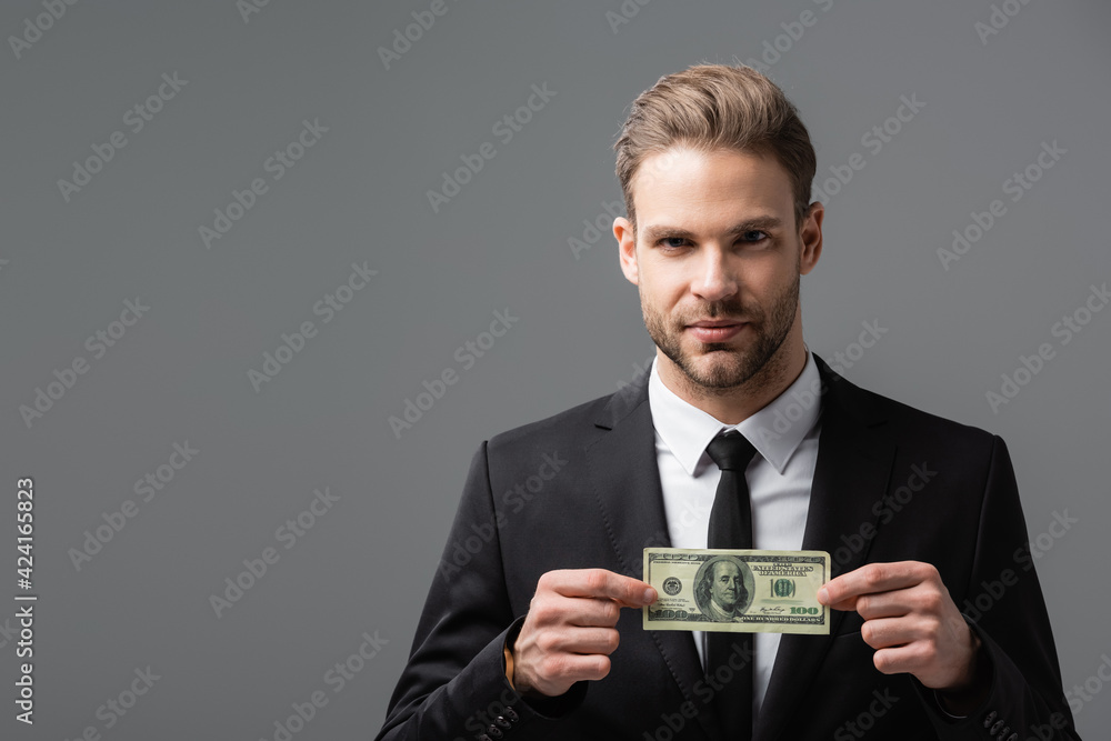 serious manager holding dollar banknote while looking at camera isolated on grey serious manager holding dollar banknote while looking at camera isolated on grey