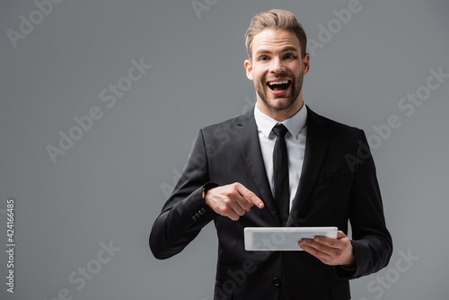 Excited manager pointing at digital tablet while looking at camera isolated on grey
