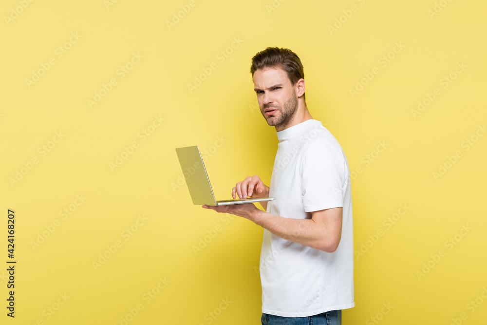 displeased man looking at camera while typing on laptop on yellow displeased man looking at camera while typing on laptop on yellow