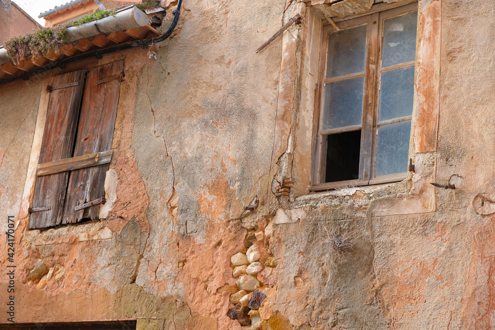 An ancient abandoned house with masonry, painted ocher, closed shutters, moss on the roof. Old window construction. Provence. France.