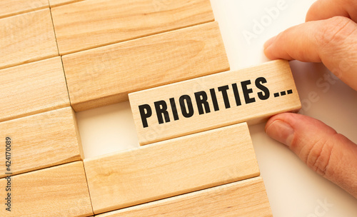 Hand holds a wooden cube with the text PRIORITIES.