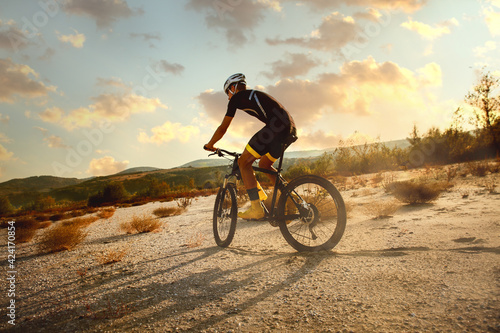 Fotografia Cyclist riding a bike trough desert on  sunset