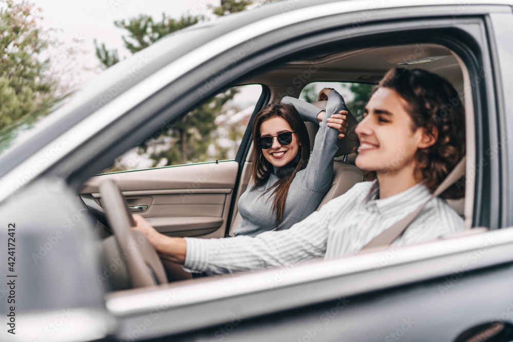 Smiling young couple in car during trip, enjoying trip, girl looking at camera