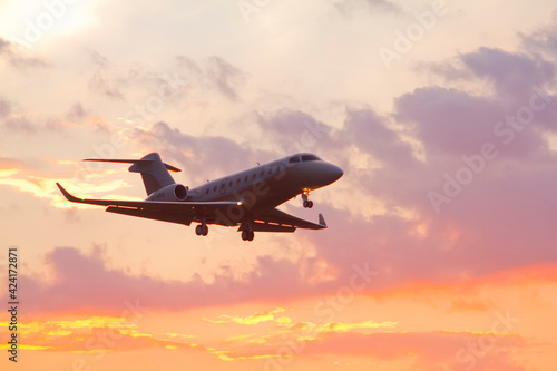 Private twin-engine jet aircraft landing at the airport with landing gear and flaps extended at sunset photo