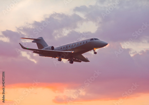 Private twin-engine jet aircraft landing at the airport with landing gear and flaps extended at sunset
