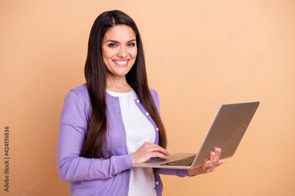 Photo of nice optimistic brunette long hairdo lady hold laptop wear purple sweater isolated on pastel beige color background Photo of nice optimistic brunette long hairdo lady hold laptop wear purple sweater isolated on pastel beige color background
