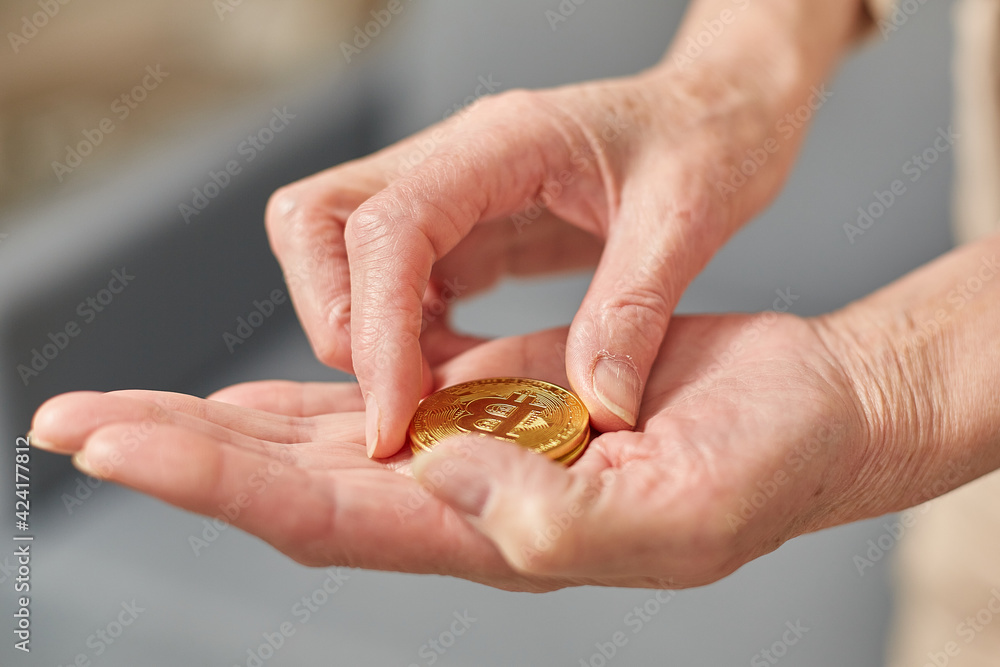 Old woman holds bitcoin coins in her hand. Senior citizen happy life concept